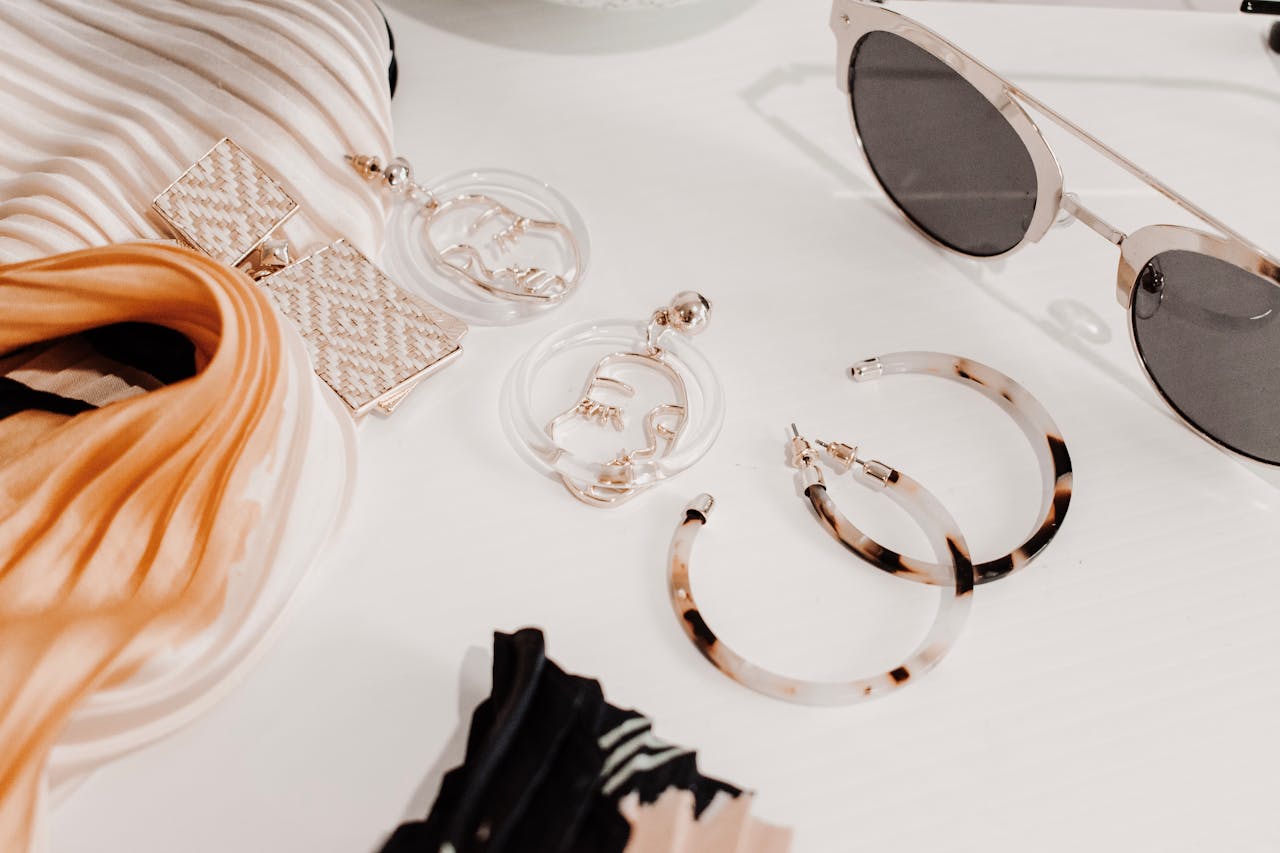 Stylish flat lay of modern fashion accessories including earrings, scarf, and sunglasses.
