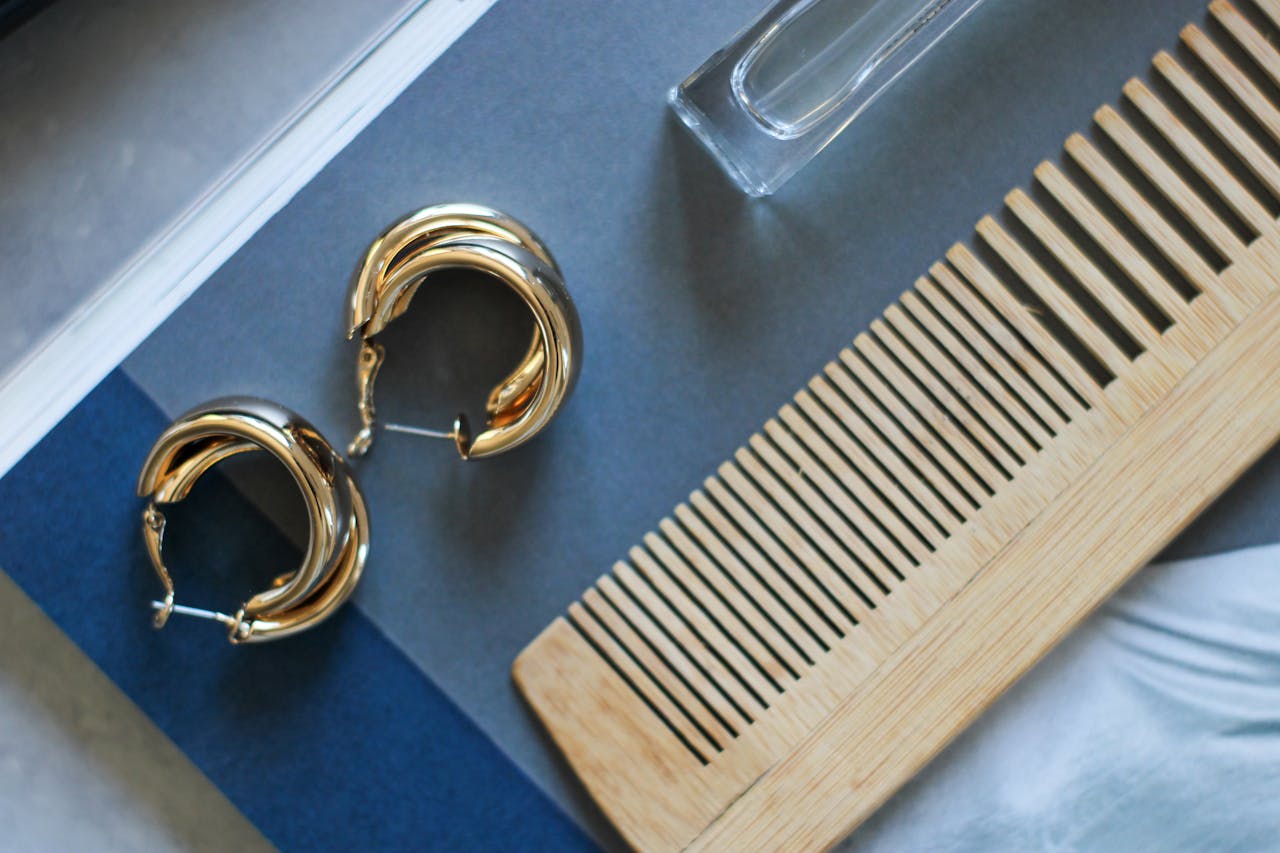 Stylish flat lay of gold hoop earrings with a wooden comb on a blue background.